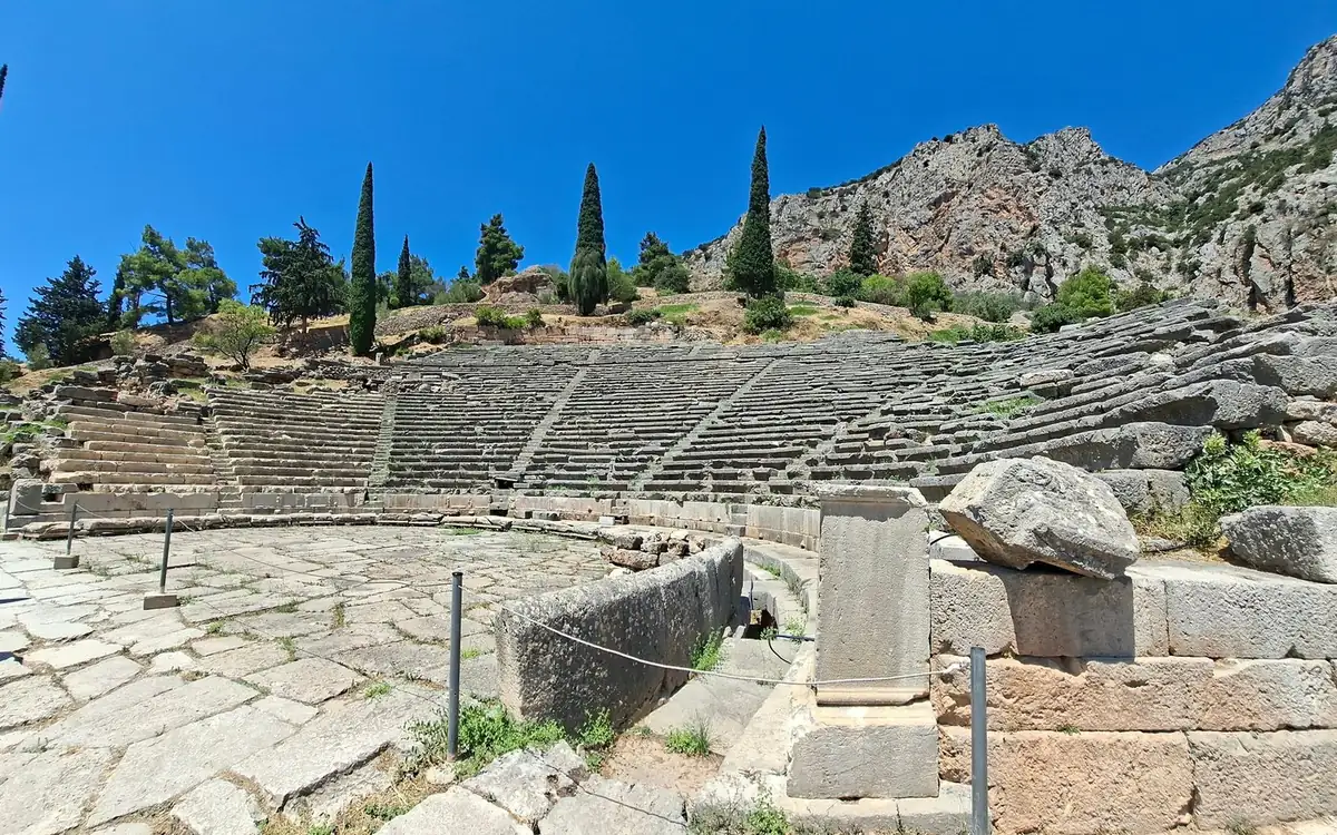 Das antike Theater von Delphi: steinerne Sitzreihen am Hang, Zypressen und graue Felsen darüber