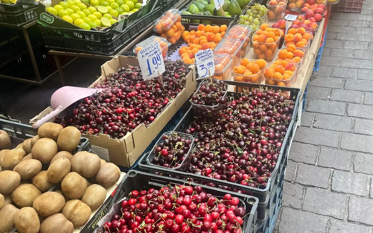 Crates of cherries, apricots, kiwis and limes on a market stall with price cards