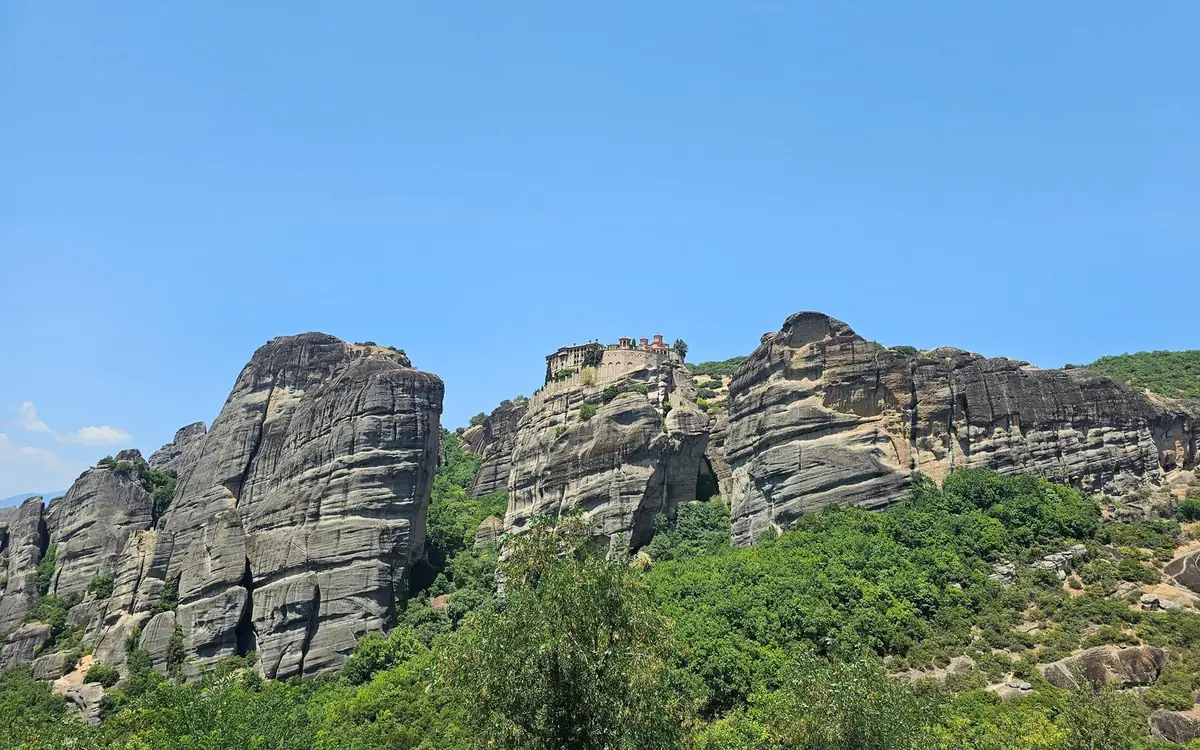 Szare skalne wieże wznoszące się nad zielonym lasem w Meteora