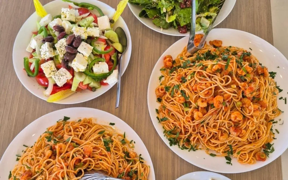 Un'insalata greca con feta e olive, un'insalata verde e due piatti di spaghetti con gamberi su un tavolo