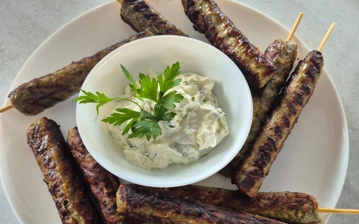 Grillowane szaszłyki na białym talerzu wokół miseczki tzatziki
