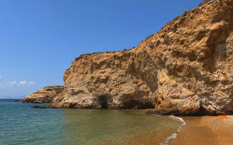 Ochrowe klify nad małą piaszczystą plażą i czystą zieloną wodą